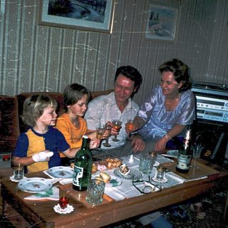 Family gathering around a table with drinks and food.