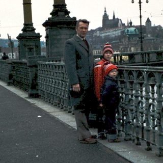Two people walking on a bridge near historic city.
