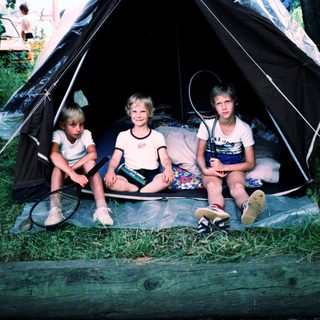Three children sitting inside a tent outdoors.