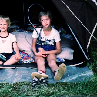 Three children sitting inside a tent outdoors.