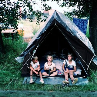 Three children sitting inside a tent outdoors.