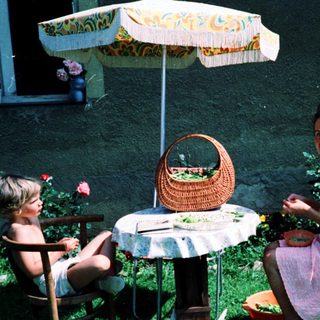 Two people, including a child, dining outdoors under umbrella.