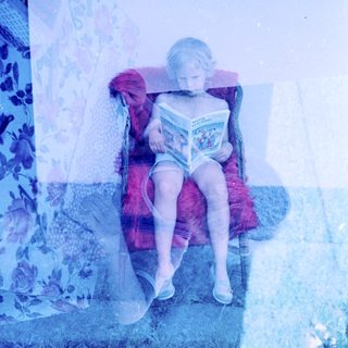 Child reading book on colorful chaise lounge.