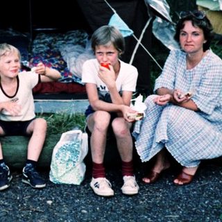 Family camping under tents in forested area.