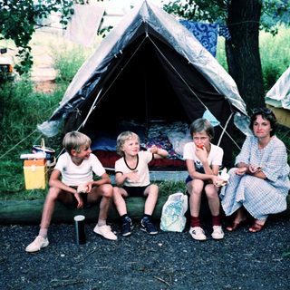 Family camping under tents in forested area.