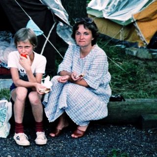Family camping under tents in forested area.