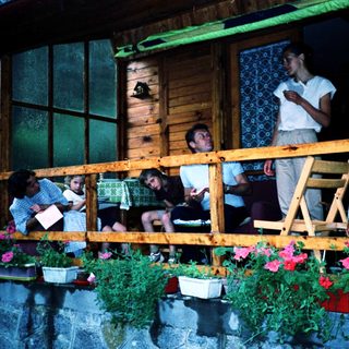 Family enjoying evening on a wooden balcony with plants.