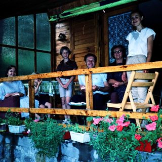 Family posing on wooden balcony with potted plants.