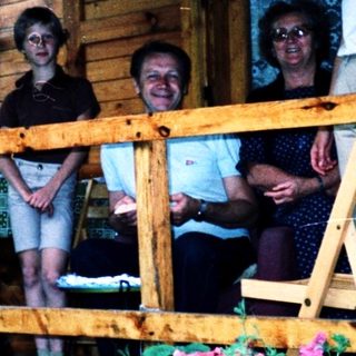 Family posing on wooden balcony with potted plants.