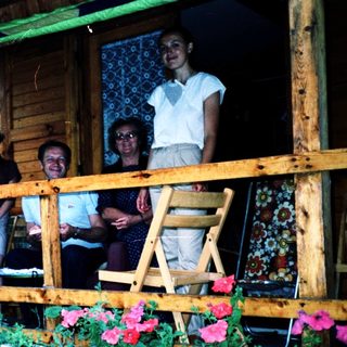 Family posing on wooden balcony with potted plants.
