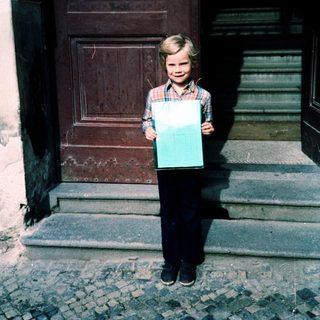 Young boy holding large turquoise sign outside door.