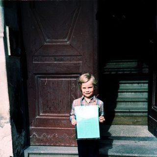 Young boy holding large turquoise sign outside door.