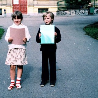 Two children holding large blank papers outdoors near a building.
