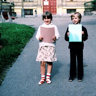 Two children holding large blank papers outdoors near a building.