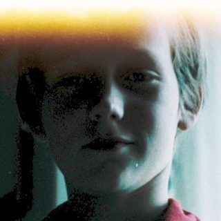 A child in a red shirt standing indoors near a window.