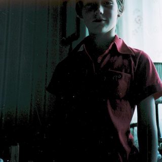 A child in a red shirt standing indoors near a window.