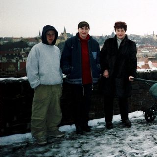 Three people standing in winter cityscape with snow, holding baby stroller.