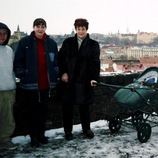 Three people standing in winter cityscape with snow, holding baby stroller.
