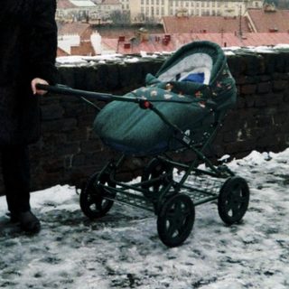 Three people standing in winter cityscape with snow, holding baby stroller.