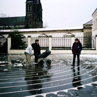 People pushing stroller in wet courtyard near church.