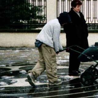 People pushing stroller in wet courtyard near church.
