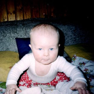 Baby sitting on bed wearing polka-dot outfit.