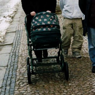 Three people walking with a baby stroller on a snowy street.