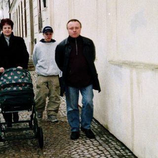 Three people walking with a baby stroller on a snowy street.