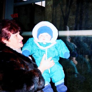 Woman holding baby in winter gear indoors.