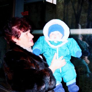 Woman holding baby in winter gear indoors.
