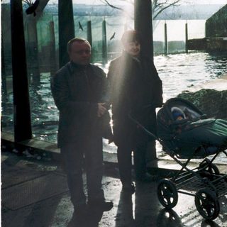 Two people standing near a stroller by a flooded outdoor area with polar bears in an enclosure.
