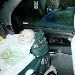 Baby secured in car seat with blanket.