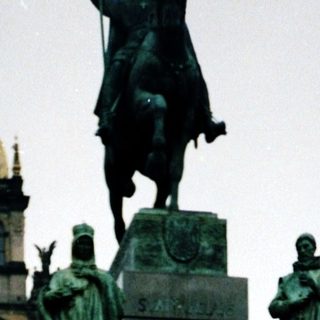 Statue square with historical monument and people.