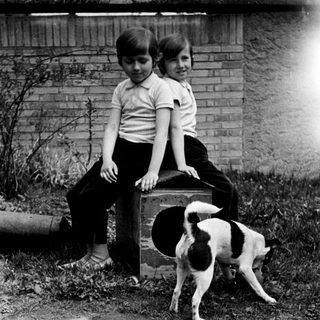 Two children and a dog near a brick wall.
