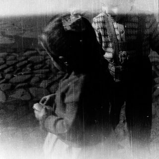 Two people embracing outdoors near water.