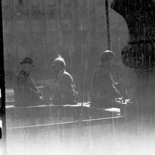 Reflection of three seated people in rainy glass.