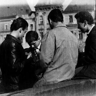 Four men sitting together outdoors, one adjusting a small device.