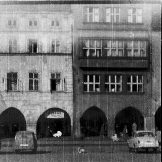 Historic European street with arched passageways and vintage vehicles.