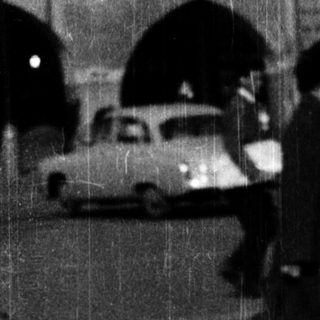 Street scene with stroller, blurred figures, and vintage cars.