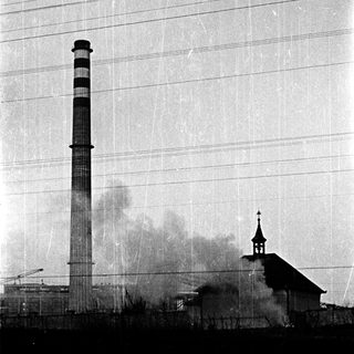 Industrial smokestack emitting smoke near church steeple.