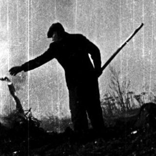 Silhouette of person shoveling rain-soaked ground.