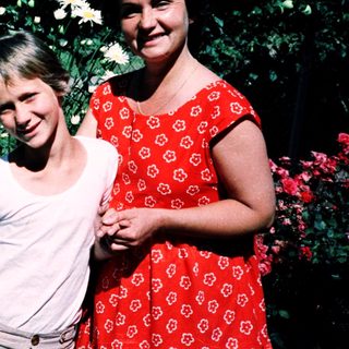 Two women posing happily with flowers outdoors.