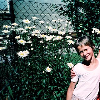 Two women posing happily with flowers outdoors.