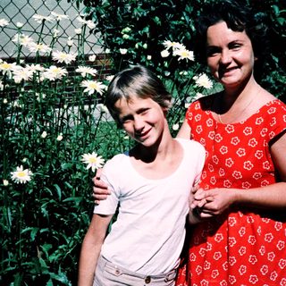 Two women posing happily with flowers outdoors.