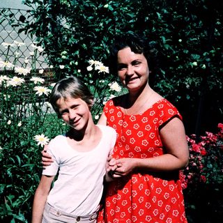 Two women posing happily with flowers outdoors.