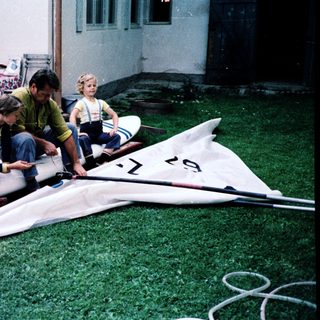 Three children assembling a windsurfing board outdoors.