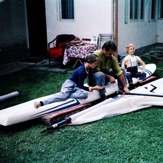 Three children assembling a windsurfing board outdoors.