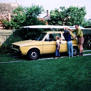 Family posing with vintage car and surfboard.