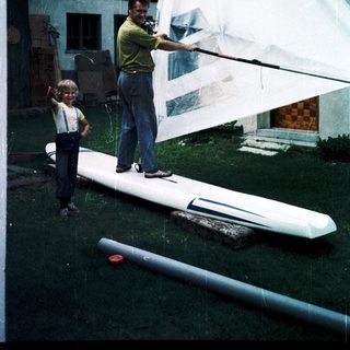 Man and child preparing sailboard with "CZ929" sail.