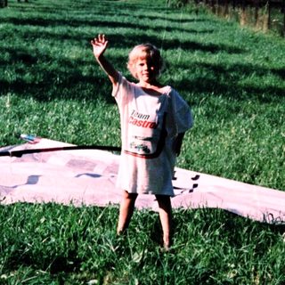 Child standing on inflatable pool in grassy field.